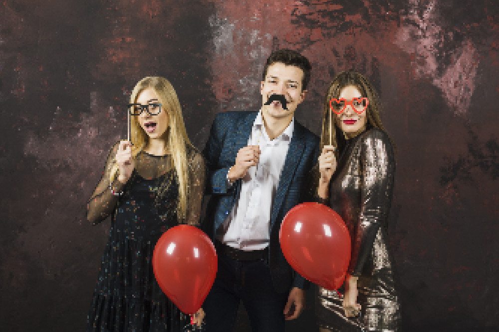 3 Personen mit Fotobox-Accessoires (Brillen, Bart) und Ballons. Geringe Auflösung, verpixelt.